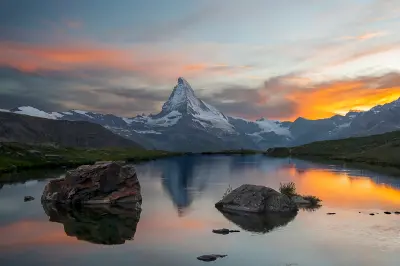 Matterhorn reflected in Stellisee at sunset with colored clouds and foreground rocks, Zermatt, Switzerland.