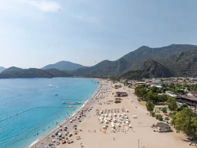 Aerial view along Ölüdeniz Beach with turquoise Mediterranean water and forested mountains near Fethiye, Türkiye.