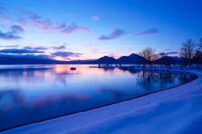 Dawn light over Lake Toya with calm water and snow-covered shoreline in Hokkaido, Japan.