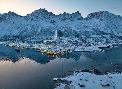 Aerial winter view of Senjahopen harbour with fishing port, village buildings, and snow-covered mountains on Senja island, Norway