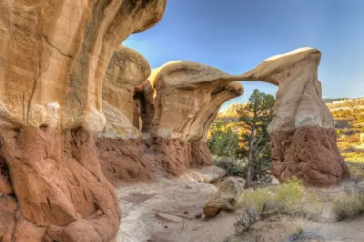 Slender Metate Arch spans between sculpted red and cream sandstone formations in the warm light at Devil’s Garden.