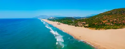Aerial panoramic view of Patara Beach, with a long golden sandy shoreline, turquoise Mediterranean water and rolling green hills extending into the distance.
