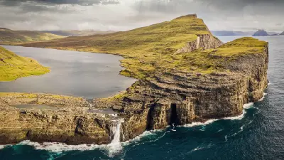 Aerial view of Bøsdalafossur waterfall on Vágar Island, Faroe Islands, where Sørvágsvatn lake drops into the Atlantic Ocean below Trælanípa cliffs.