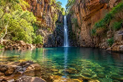 Waterfall cascading between towering red sandstone cliffs into the clear emerald pool at Emma Gorge.