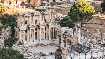 Elevated view of the Library of Celsus façade surrounded by columns, stone ruins, and trees at Ephesus, Turkey.