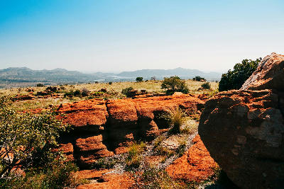 Red quartzite rock formations on the Magaliesberg plateau with grassland and distant hills in the background.