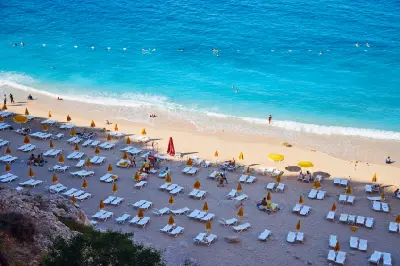 Elevated view of Kaputaş Beach, with white sun loungers and yellow umbrellas lining the sandy shore as swimmers enjoy vivid turquoise Mediterranean water.