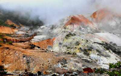 Steaming volcanic terrain with mineral-colored slopes and a wooden walkway in Jigokudani Hell Valley, Noboribetsu, Hokkaido.
