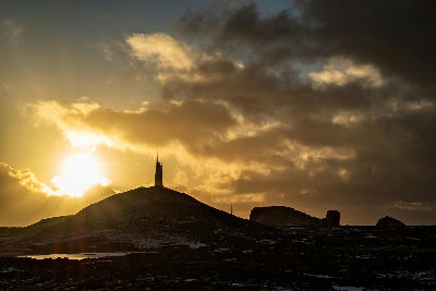 Silhouette of Reykjanesviti lighthouse against a golden sunset sky on the Reykjanes Peninsula, Iceland.