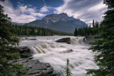 Athabasca Falls flowing through a rocky canyon with forest and mountain backdrop in Jasper National Park, Alberta, Canada