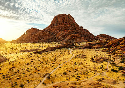 Granite mountain formations rising above desert plains at Spitzkoppe in Namibia under textured clouds and warm light.