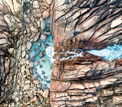 Aerial view of Injidup Natural Spa showing turquoise seawater flowing between fractured granite rocks and boulders in Western Australia.