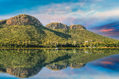Magaliesberg mountains reflected in Hartbeespoort Dam beneath a colourful sky in North West Province, South Africa.