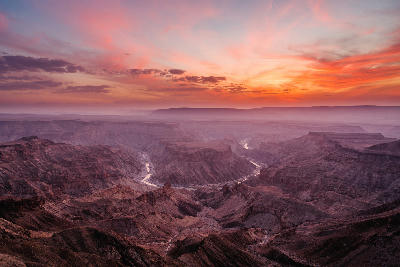Panoramic view of Fish River Canyon at sunset, with deep rocky gorges, winding river channels and layers of rugged cliffs illuminated beneath a colourful evening sky in southern Namibia.