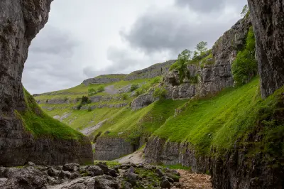 View from inside Gordale Scar showing steep limestone cliffs, green slopes and scattered boulders beneath a cloudy sky in North Yorkshire.