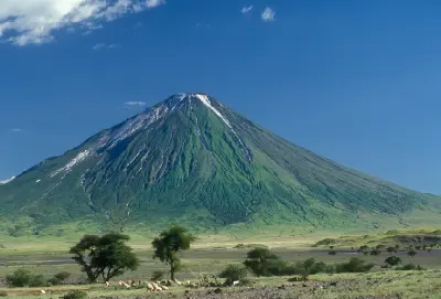 Ol Doinyo Lengai volcano towering above the savanna near Lake Natron in northern Tanzania, with green volcanic slopes beneath a deep blue sky.