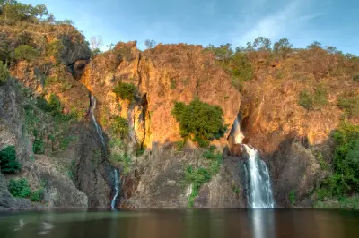 Twin waterfalls descending sunlit rocky cliffs into a calm plunge pool at Wangi Falls in Litchfield National Park, Northern Territory, Australia.
