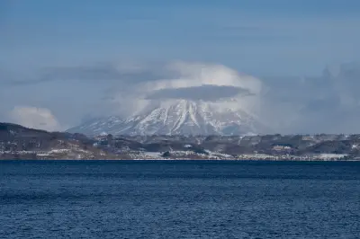 Mount Usu rising above Lake Toya with snow-covered slopes and cloud cover in Hokkaido, Japan.