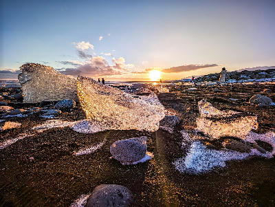 Large glacial ice chunks on the black sand of Diamond Beach on Iceland’s South Coast at sunset, with golden light reflecting through the ice.