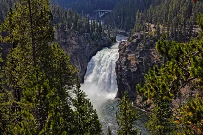 Upper Falls of the Yellowstone River framed by pine trees with bridge visible upstream