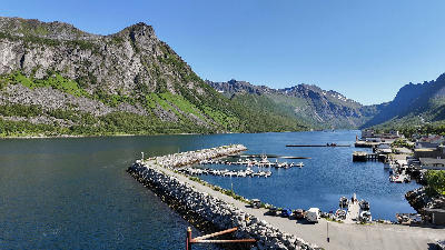 Gryllefjord harbour forms a sheltered basin behind a stone breakwater, with small boats, ferry infrastructure, and steep mountain walls enclosing the fjord.