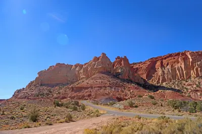 Burr Trail Road curves toward towering red and cream sandstone cliffs near the upper entrance to Long Canyon in southern Utah.