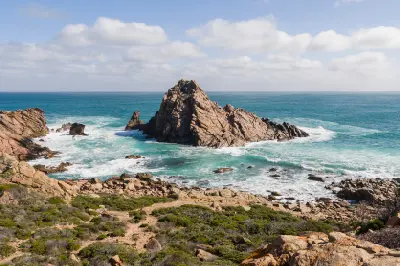 Sugarloaf Rock rising from turquoise ocean and breaking surf along the rocky Margaret River coast of Western Australia.