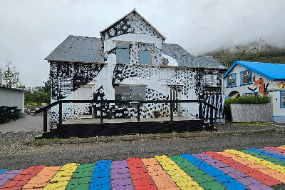 Colorful rainbow street leading past a mural-covered wooden building in Seyðisfjörður in the Eastfjords of Iceland.