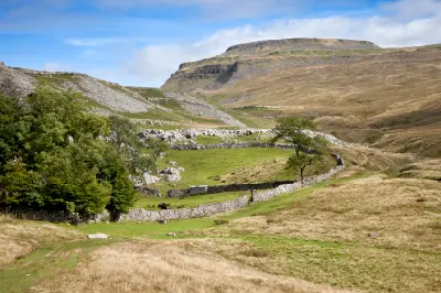 Ingleborough mountain overlooking green pastures, limestone slopes and winding dry-stone walls in the Yorkshire Dales, England.