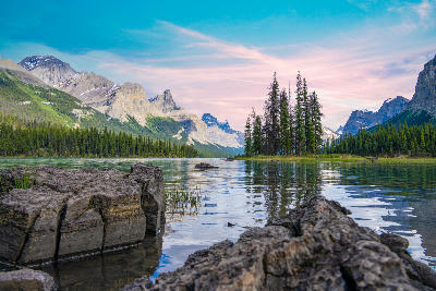 Spirit Island on Maligne Lake at sunset with turquoise water, rocky foreground, and surrounding mountain peaks in Jasper National Park