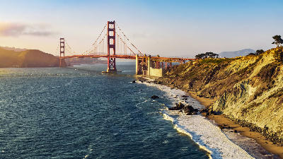 Aerial view of the Golden Gate Bridge at sunset with rugged California coastline and waves along the shore