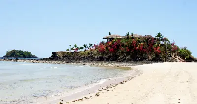 White sand beach and tropical volcanic shoreline on Nosy Be island in Madagascar with calm turquoise Indian Ocean water and coastal vegetation.