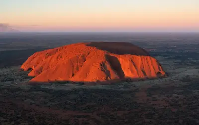 Aerial view of Uluru glowing red in evening light above the surrounding desert in Uluru-Kata Tjuta National Park, Australia.