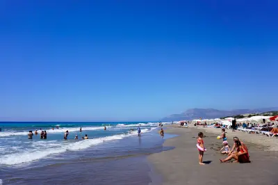 Visitors swimming and relaxing along the broad sandy shoreline of Patara Beach, with gentle Mediterranean waves beneath a clear blue summer sky.