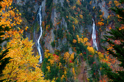 Twin waterfalls of Ginga and Ryusei flowing down steep cliffs surrounded by autumn foliage in Sounkyo Gorge, Hokkaido, Japan.