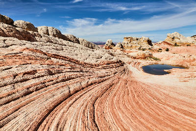 Swirling sandstone layers at White Pocket in Vermilion Cliffs National Monument, Northern Arizona, with smooth white and red rock formations and a small desert pool.