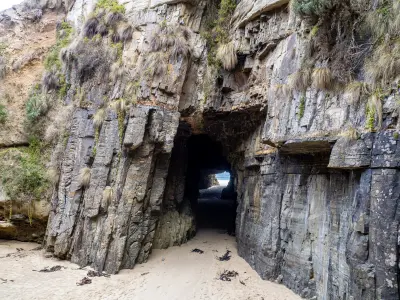 Sand and layered rock walls inside Remarkable Cave with the ocean visible through the opening, Tasmania.