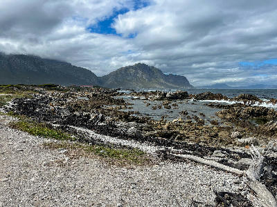 Rocky shoreline and tidal pools along Walker Bay beneath storm clouds near Hermanus in the Western Cape, South Africa