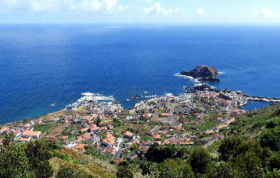 Aerial view of Porto Moniz natural pools in Madeira, showing lava rock formations, coastal village rooftops, and the Atlantic Ocean.