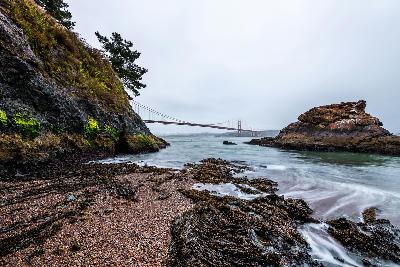 Dawn view of Golden Gate Bridge from Kirby Cove with foggy bay and rocky beach