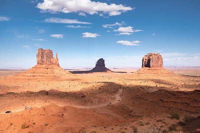 Cars driving along dirt road in Monument Valley with iconic buttes under blue sky and desert landscape