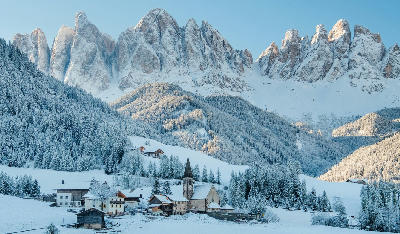 Snow-covered village in Val di Funes with the Dolomites mountains in the background, South Tyrol, Italy.