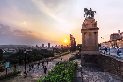 Sunset view from the Union Buildings in Pretoria, with the equestrian statue overlooking terraced gardens and the city skyline glowing beneath a colourful evening sky.