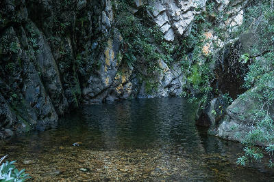 Still mountain pool beneath rocky gorge cliffs at Rust-en-Vrede Waterfall near Oudtshoorn in the Western Cape of South Africa.