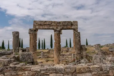 Stone Byzantine gateway surrounded by ancient ruins and tall cypress trees at Hierapolis in Pamukkale, Turkey.