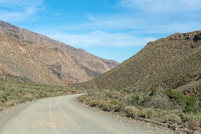 Gravel road curving through dry mountain valleys in Seweweekspoort near Laingsburg, Klein Karoo, South Africa.