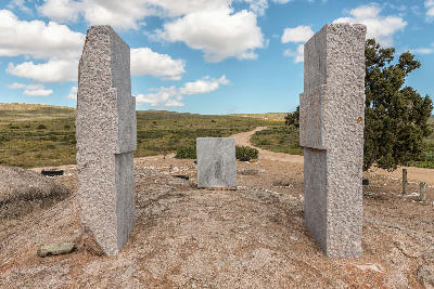 Stone monument dedicated to Vasco da Gama on a granite outcrop in St Helena Bay, surrounded by coastal shrubland, dirt roads and open West Coast landscapes beneath a blue sky with scattered clouds.