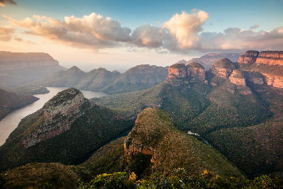 Panoramic view of Blyde River Canyon at sunrise, showing dramatic sandstone cliffs, deep valleys, winding river channels and layered mountain ridges in Mpumalanga, South Africa.