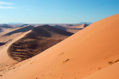 Layered orange sand dunes with sharp shadow lines in the Namib Desert near Sossusvlei, Namibia.