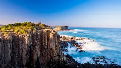 Dramatic columnar cliffs and an offshore sea stack surrounded by blue ocean at Minnamurra Point on the Illawarra Coast.